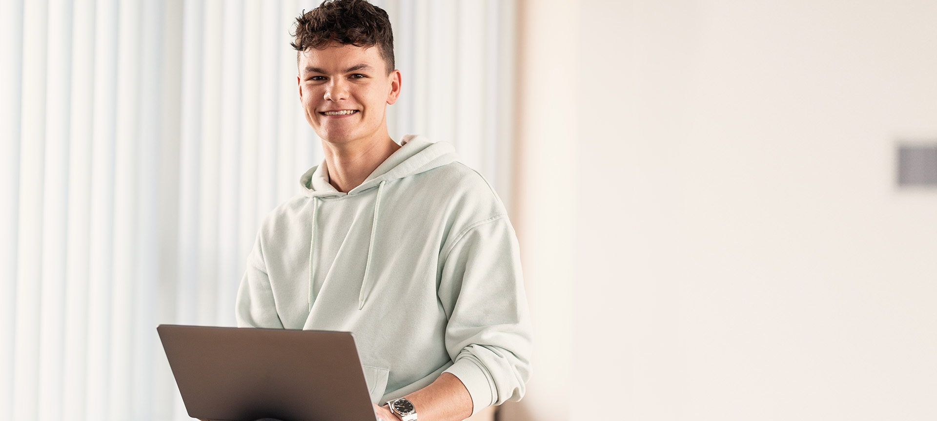 Smiling apprentice with curly hair in a mint hoodie working on a laptop