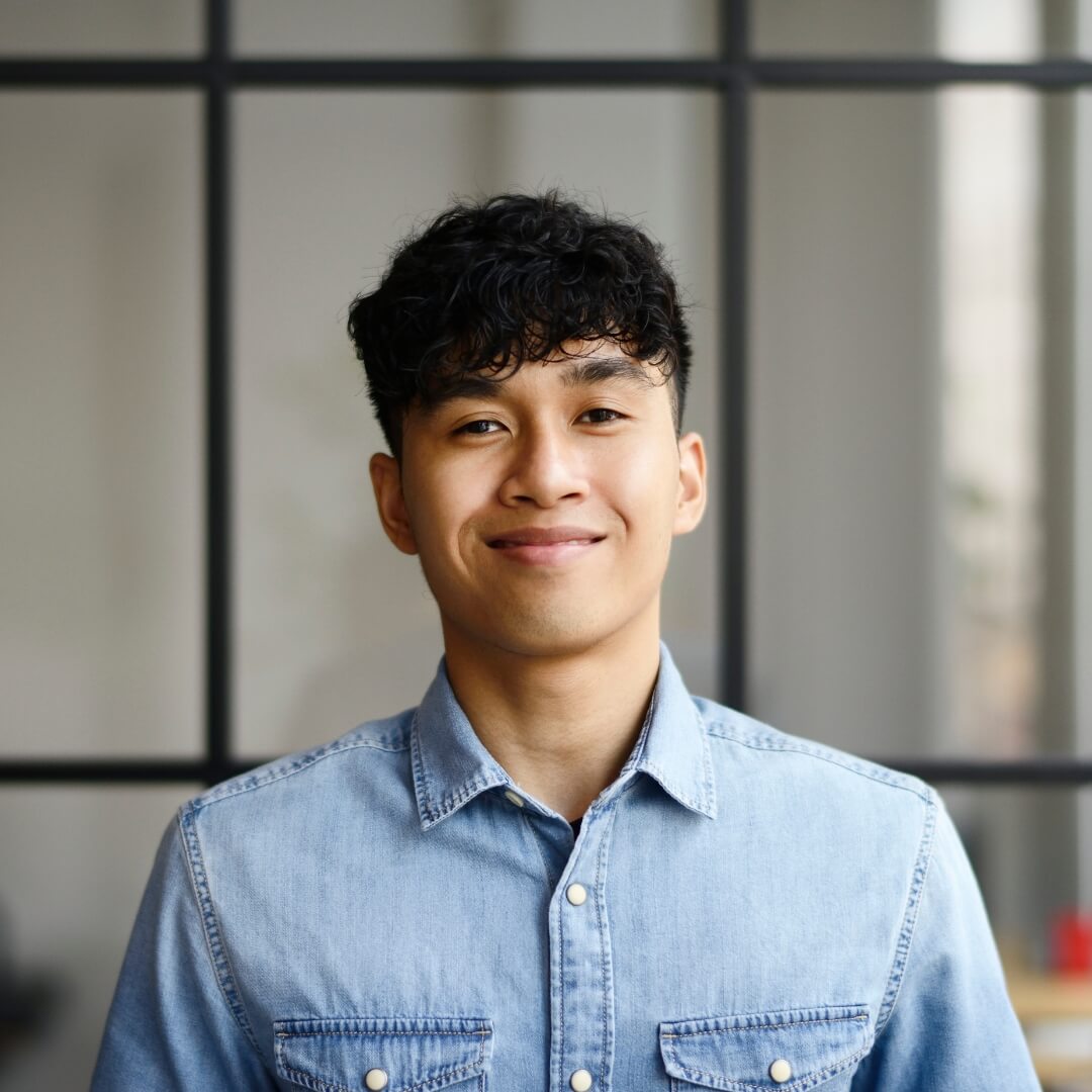 A smiling apprentice in a denim shirt standing in front of a glass wall