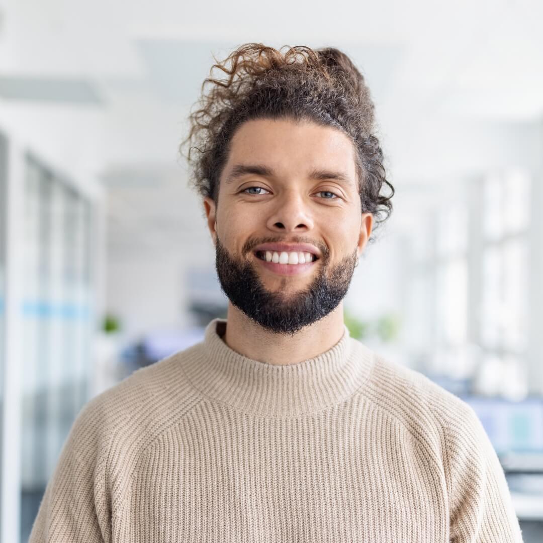 A smiling young professional in a beige sweater in a bright, open-concept office