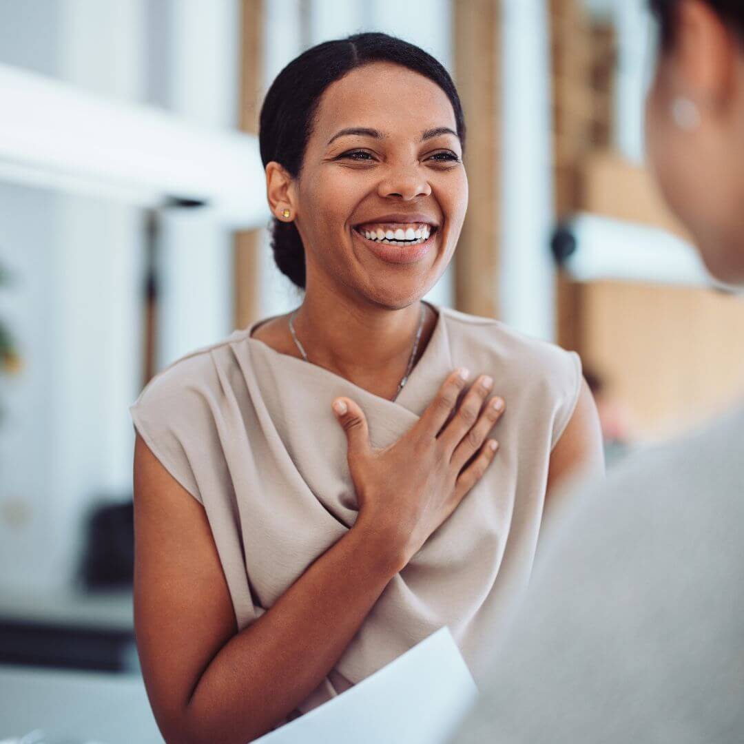 Laughing woman with her hand on her heart talking to a colleague in an office