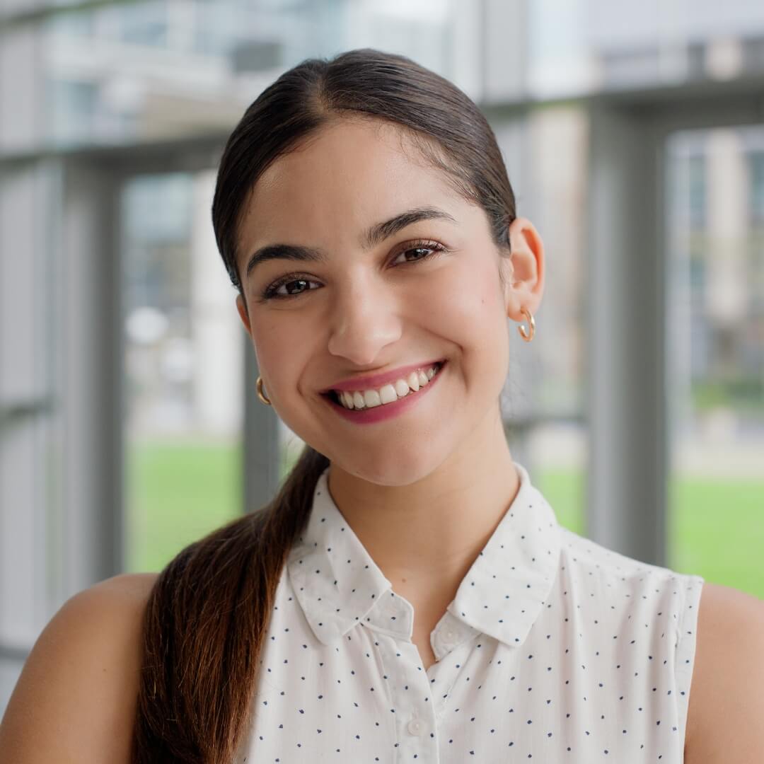 A smiling student in a white blouse in front of large windows