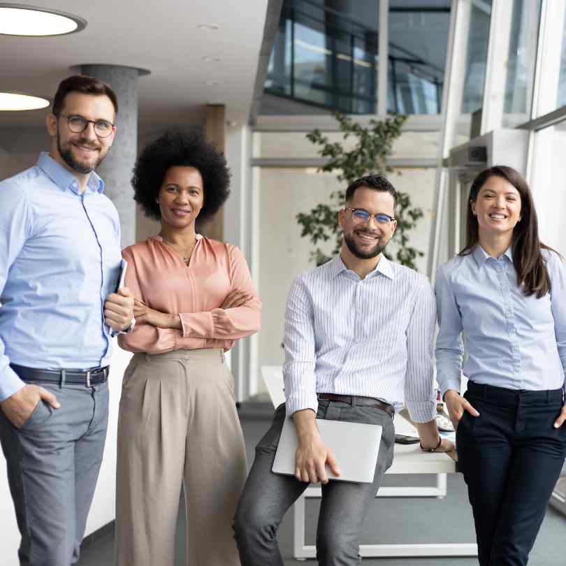 Four smiling colleagues standing together in a bright, modern office