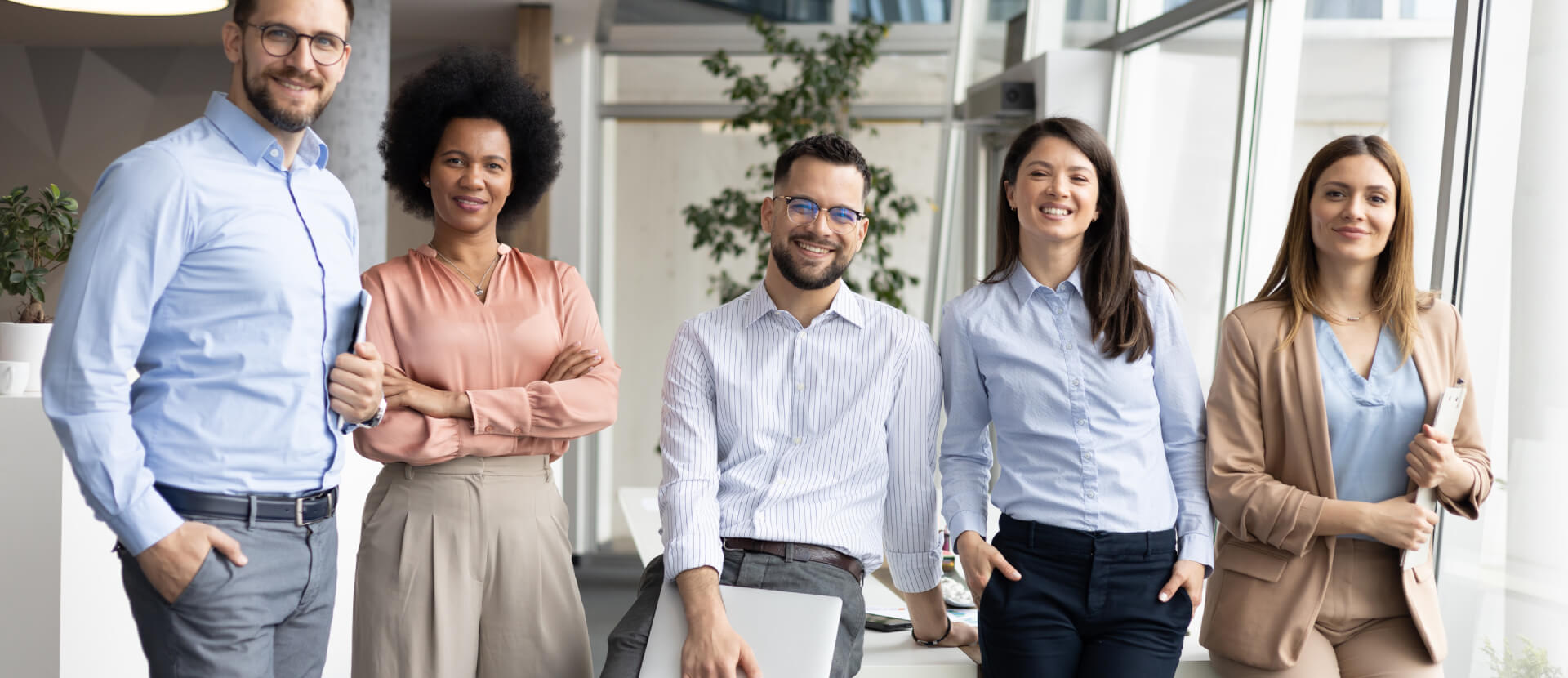 Fünf lächelnde Kolleginnen und Kollegen stehen gemeinsam in einem hellen, modernen Büro