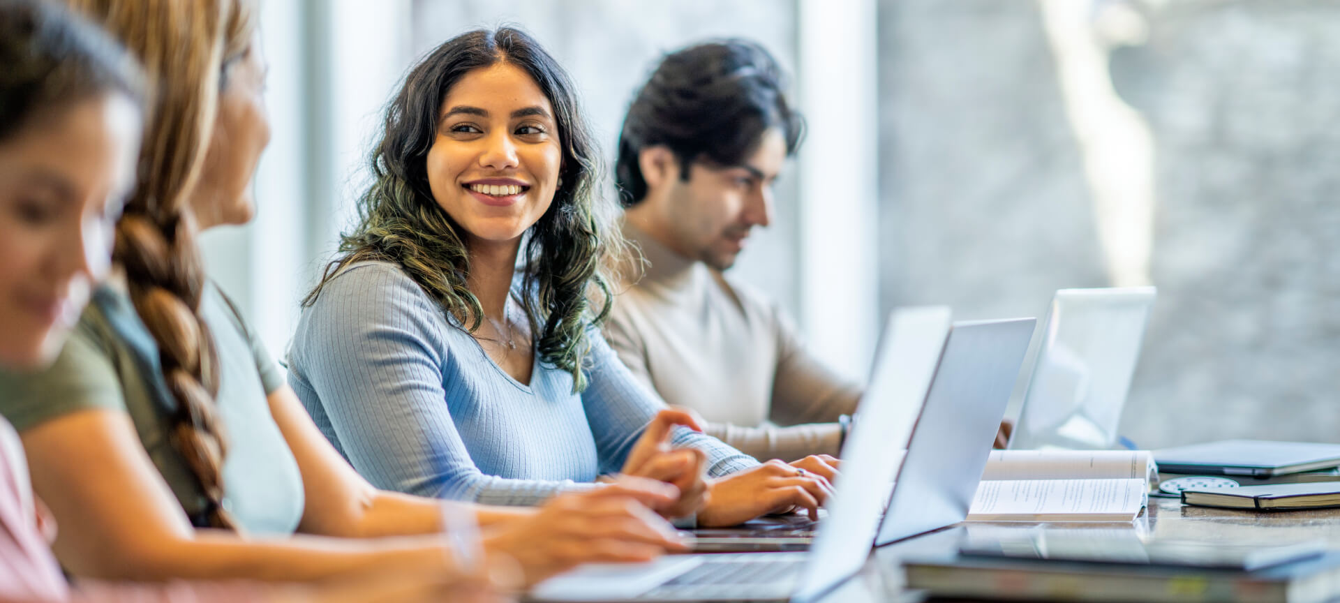 Lächelnde Werkstudentin am Laptop, neben ihr arbeiten Kolleginnen und Kollegen am Tisch