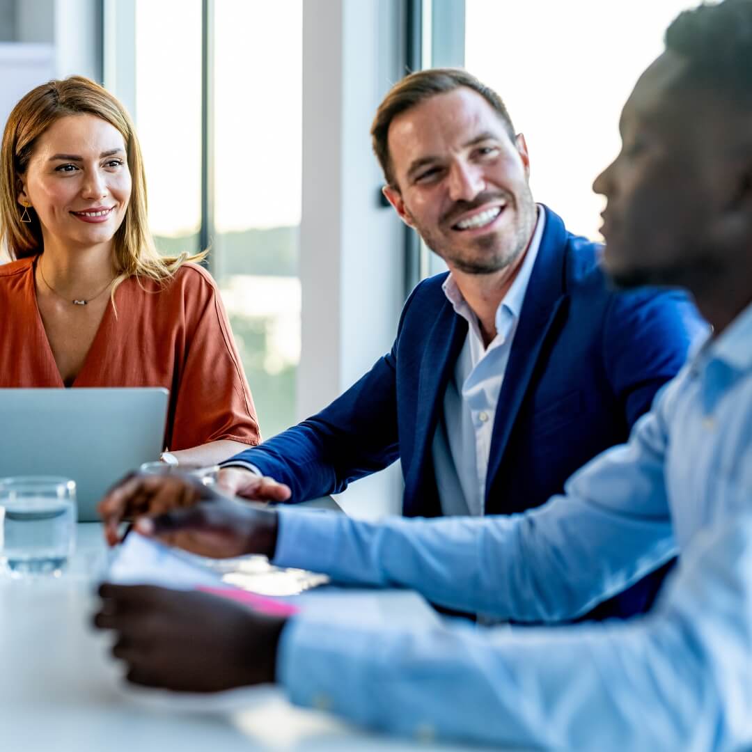 Zwei Kollegen und eine Kollegin unterhalten sich lächelnd in einem hellen Besprechungsraum